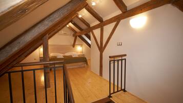 A wooden loft bedroom with a sloped ceiling, a bed, and a small seating area.