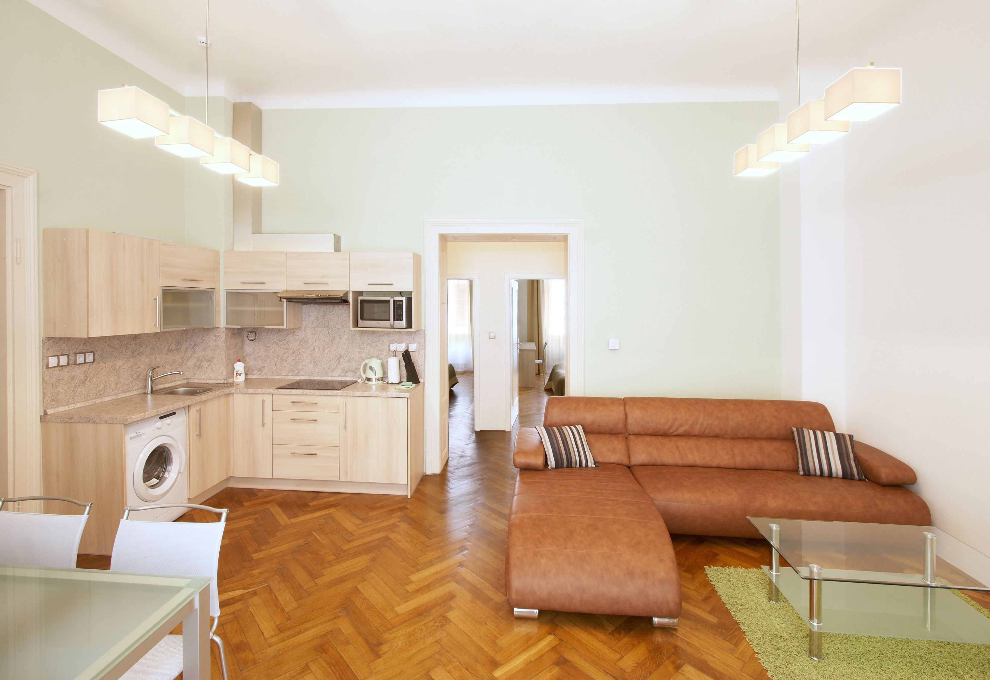A modern kitchen with a washing machine, a microwave, and a dining area with a glass table.