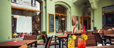 An outdoor dining area with wooden tables and chairs, a menu board, and a restaurant sign.