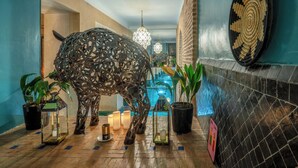 A hallway with a decorative metal sculpture resembling a bull, potted plants, candles, and a tiled wall with a geometric pattern. - Riad Ines Home (Marrakech)