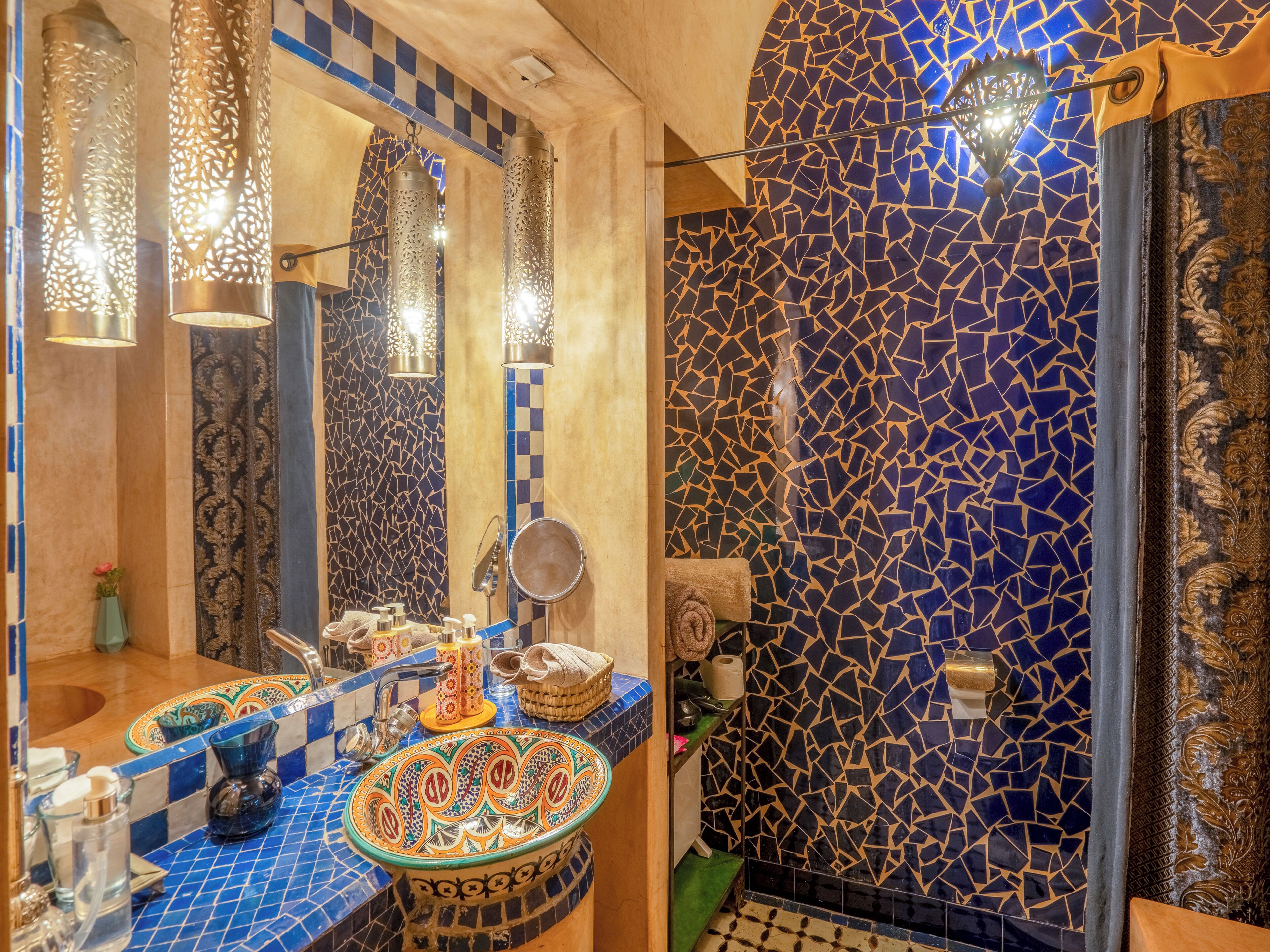 A bathroom with a blue mosaic wall, a sink with ornate tiles, and hanging lights.