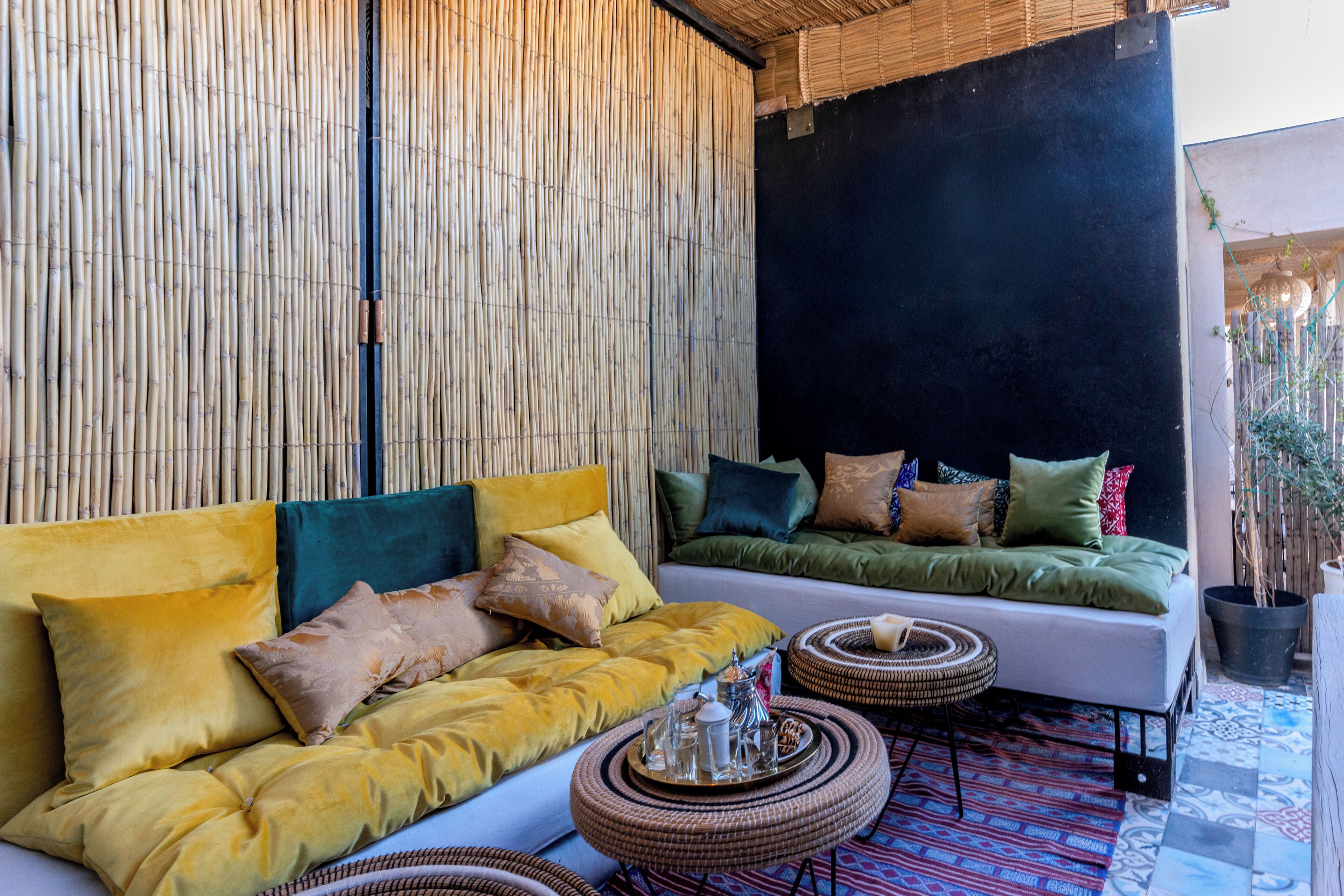 Un espacio exterior moderno con zona de estar, sofá y cojines, una mesa de centro tejida y un muro de bambú.