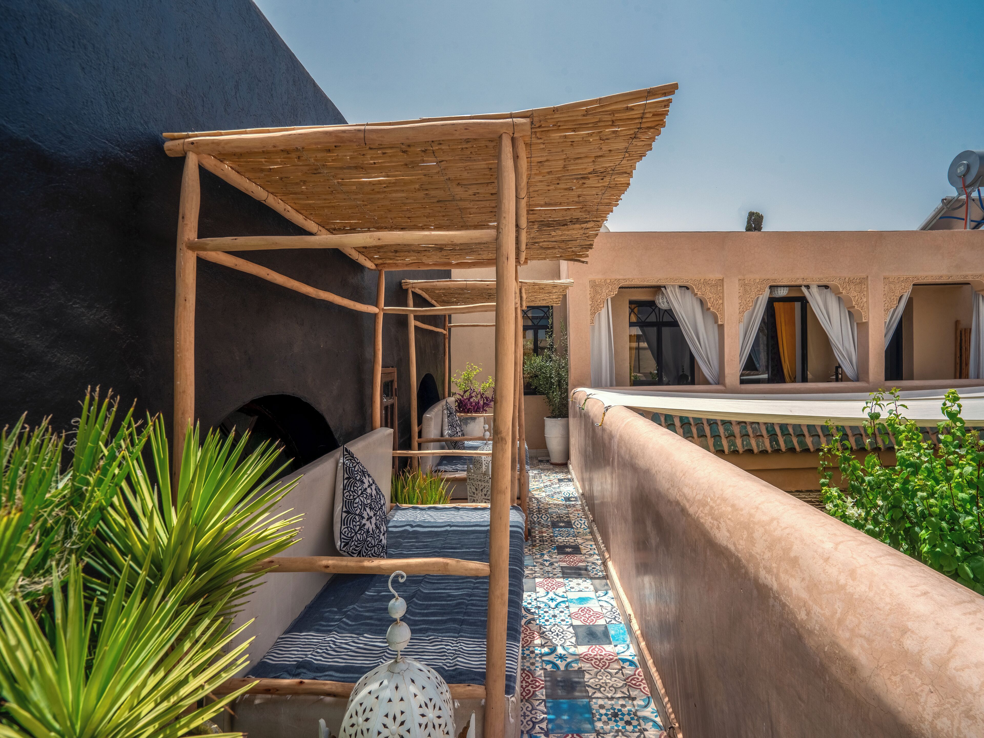 A cozy outdoor seating area with a wooden pergola, patterned cushions, and a decorative lantern.