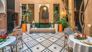 A courtyard with a tiled floor, a central seating area with a table set for dining, and potted plants. - Riad Ines Home (Marrakech)