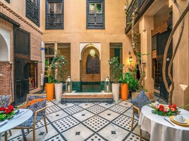 Un cortile con pavimento piastrellato, zona salotto centrale con tavolo apparecchiato per la cena e piante in vaso.
