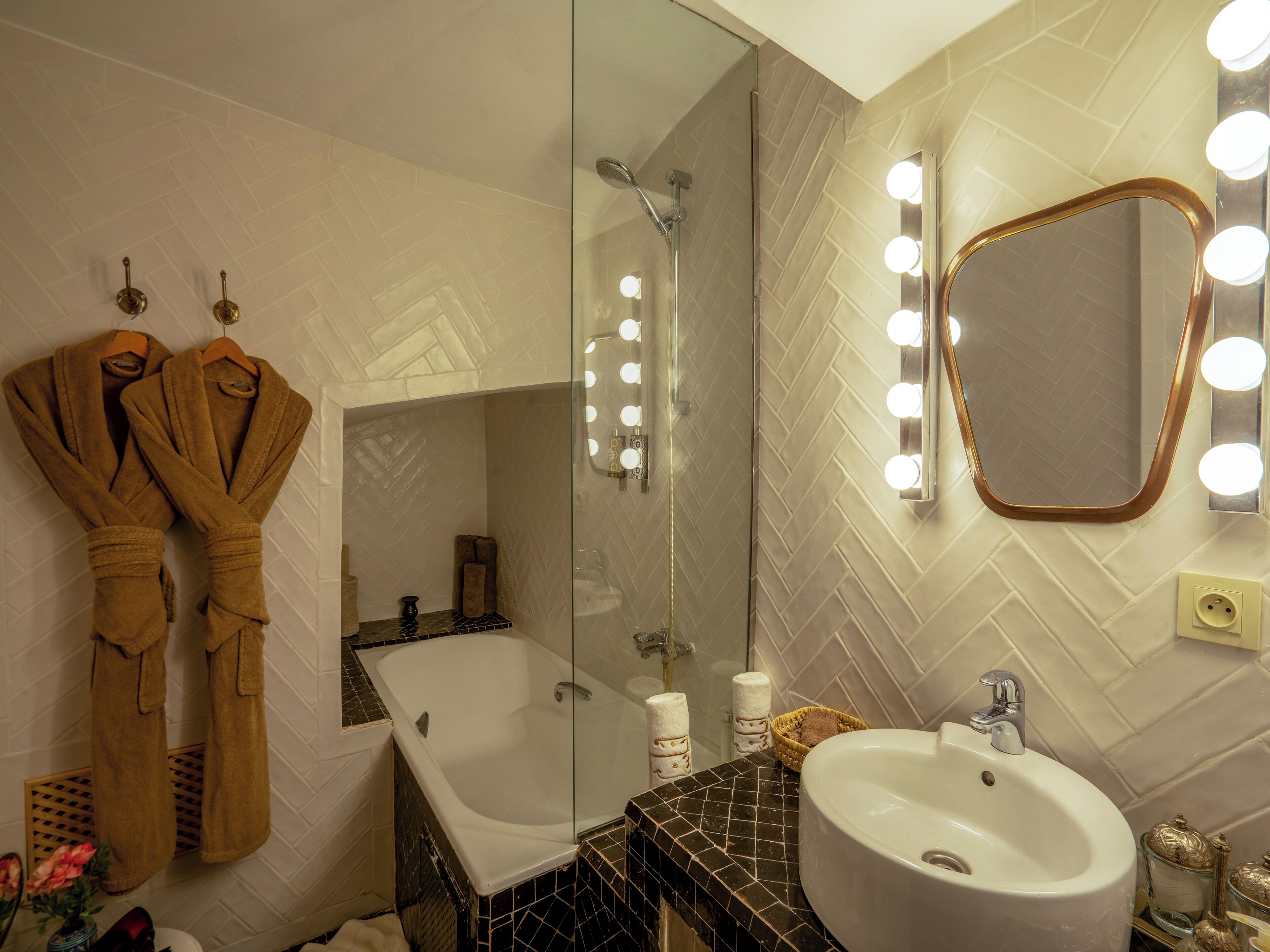 Une salle de bain avec une baignoire, un lavabo et un miroir avec éclairage. Des serviettes et des peignoirs sont accrochés à des crochets.