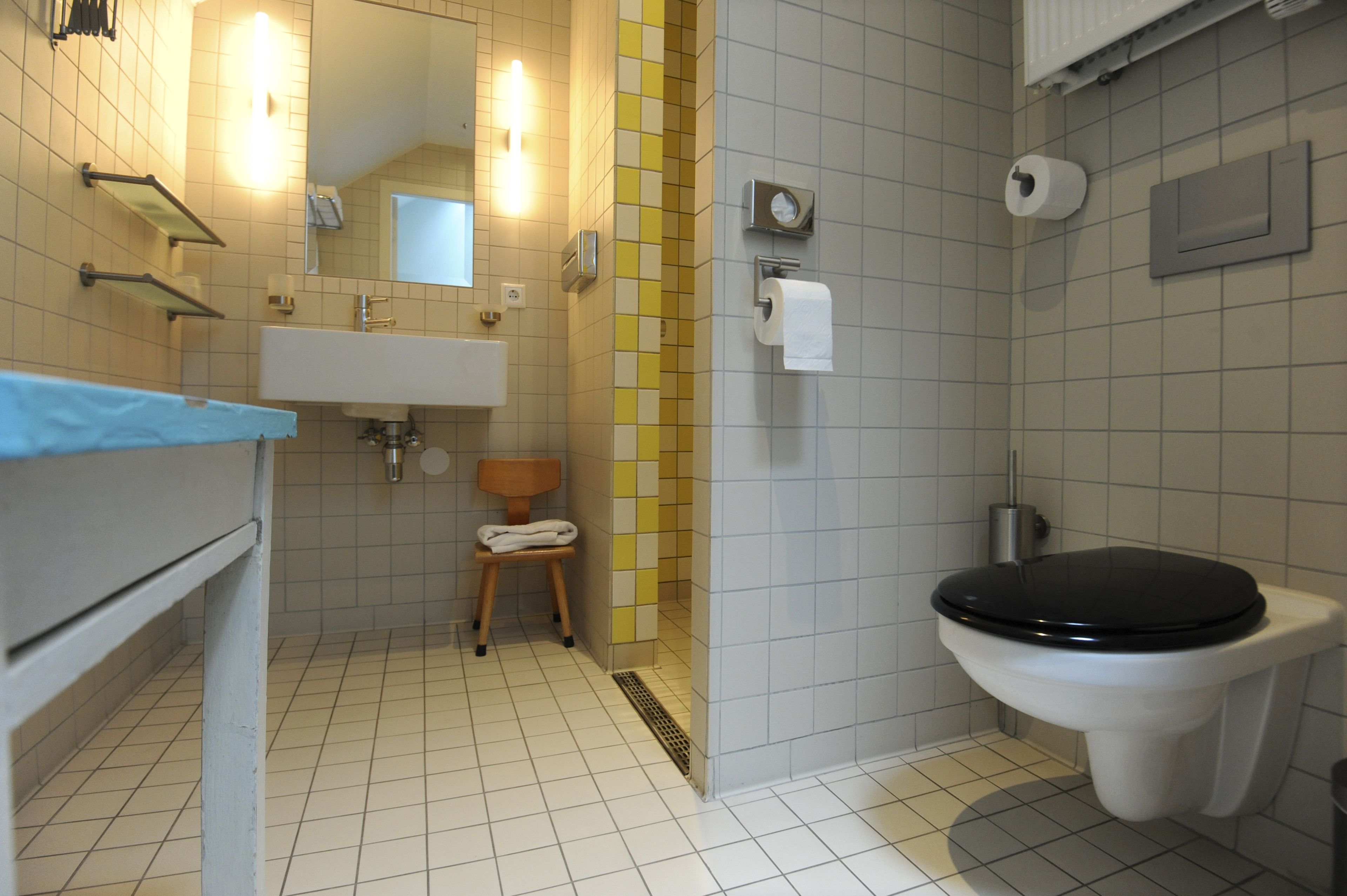 Un bagno con il water, un lavandino, uno specchio, un porta asciugamani e un piccolo sgabello di legno.