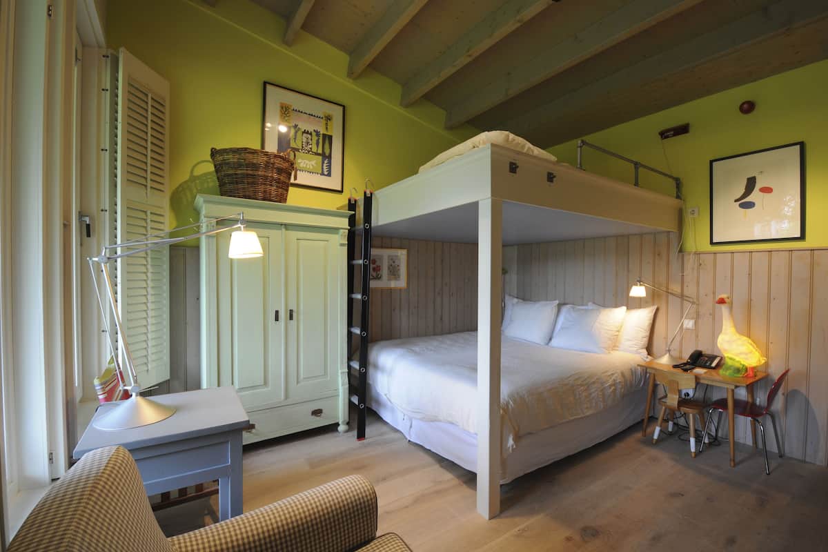 Una habitación con una cama litera, un escritorio con lámpara, una silla y una mesita.
