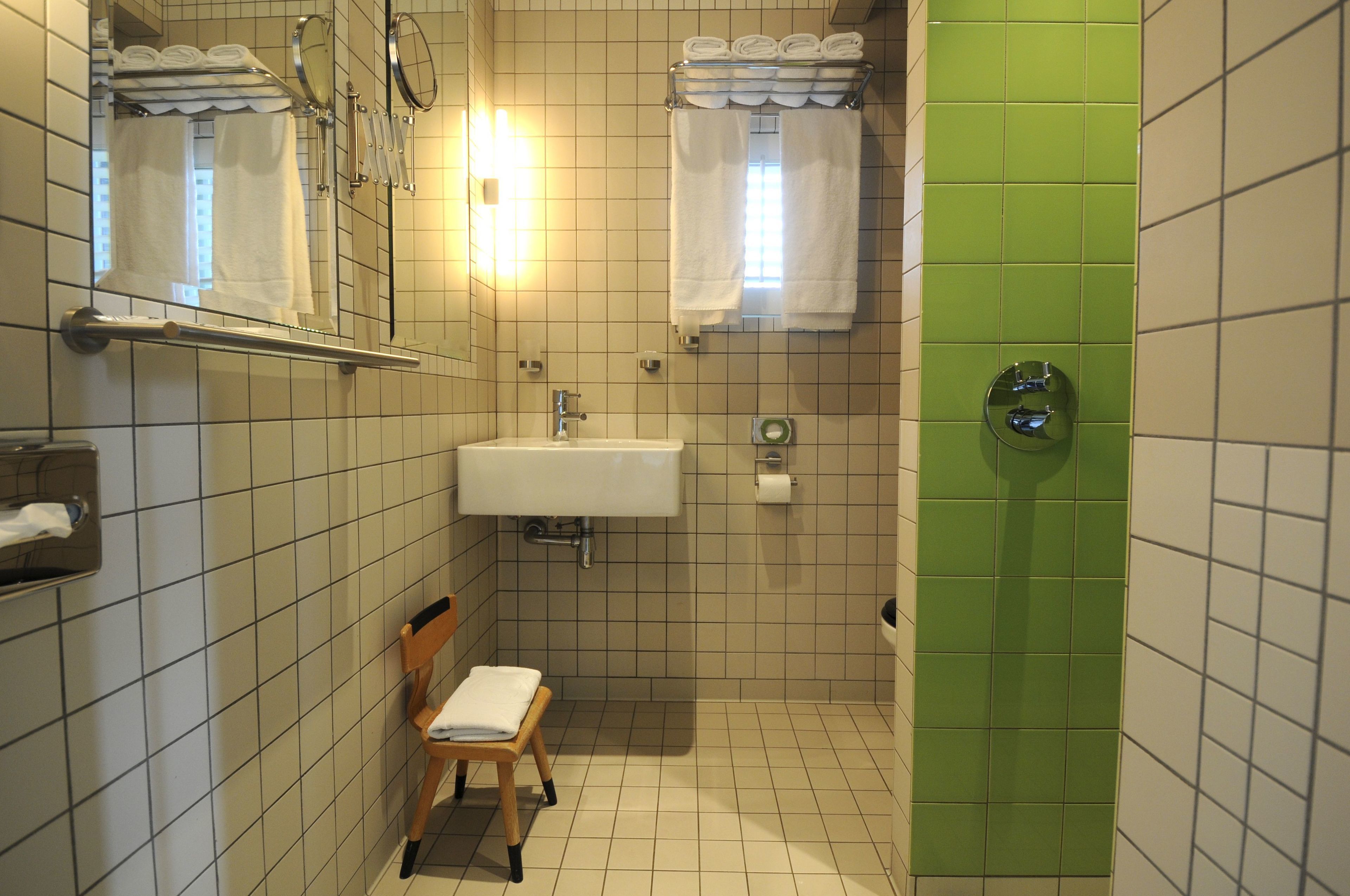 Un baño con lavamanos, espejo, toallero y una zona de ducha con azulejos verdes.