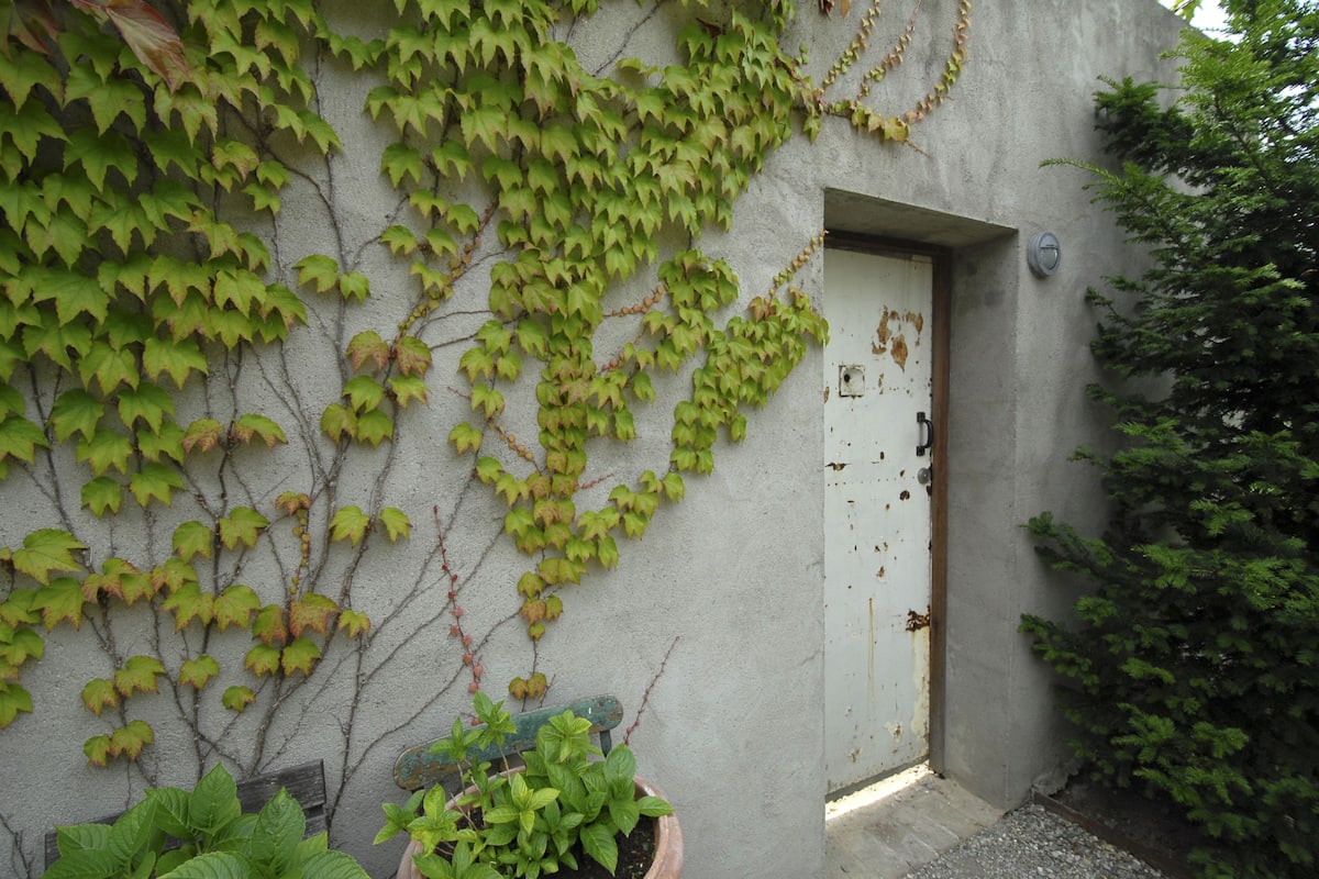 Un edificio con fachada de concreto, una puerta blanca y hiedra verde cubriendo las paredes.