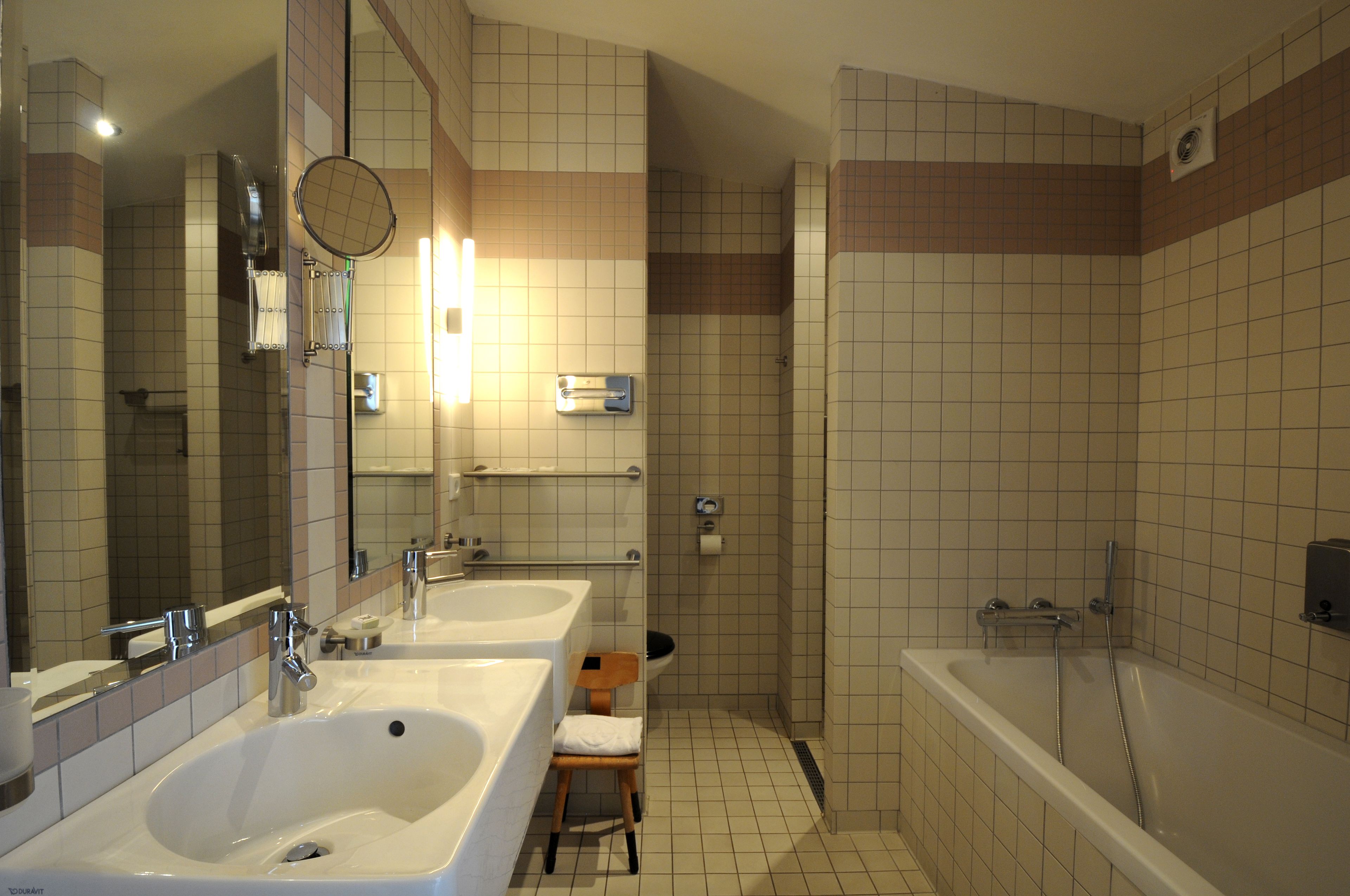 A bathroom with two sinks, a mirror, a shower, and a toilet.