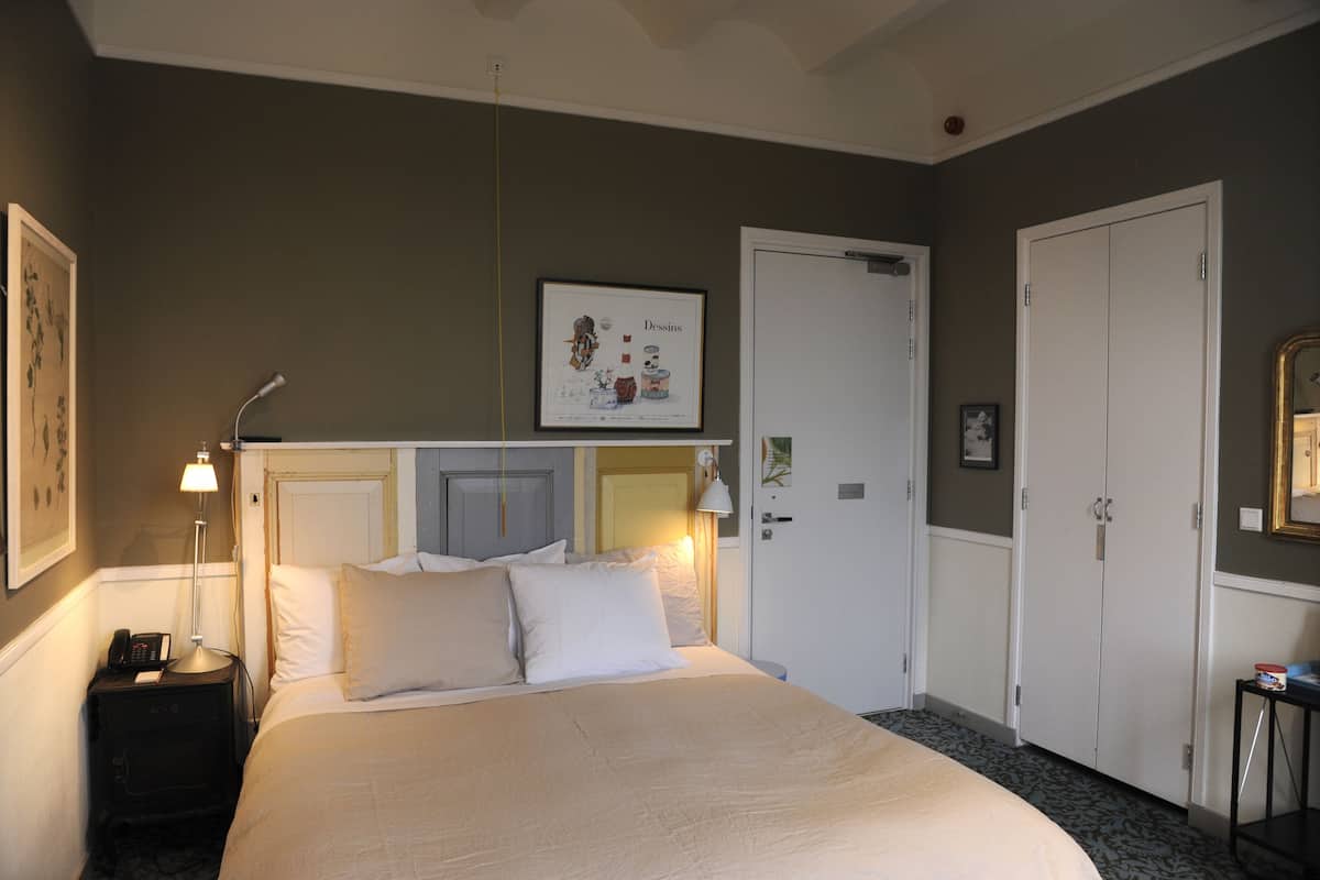 Habitación de hotel con cama, mesita de noche, lámpara, armario y un cuadro en la pared.