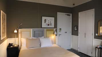 Habitación de hotel con cama, mesita de noche, lámpara, armario y un cuadro en la pared.