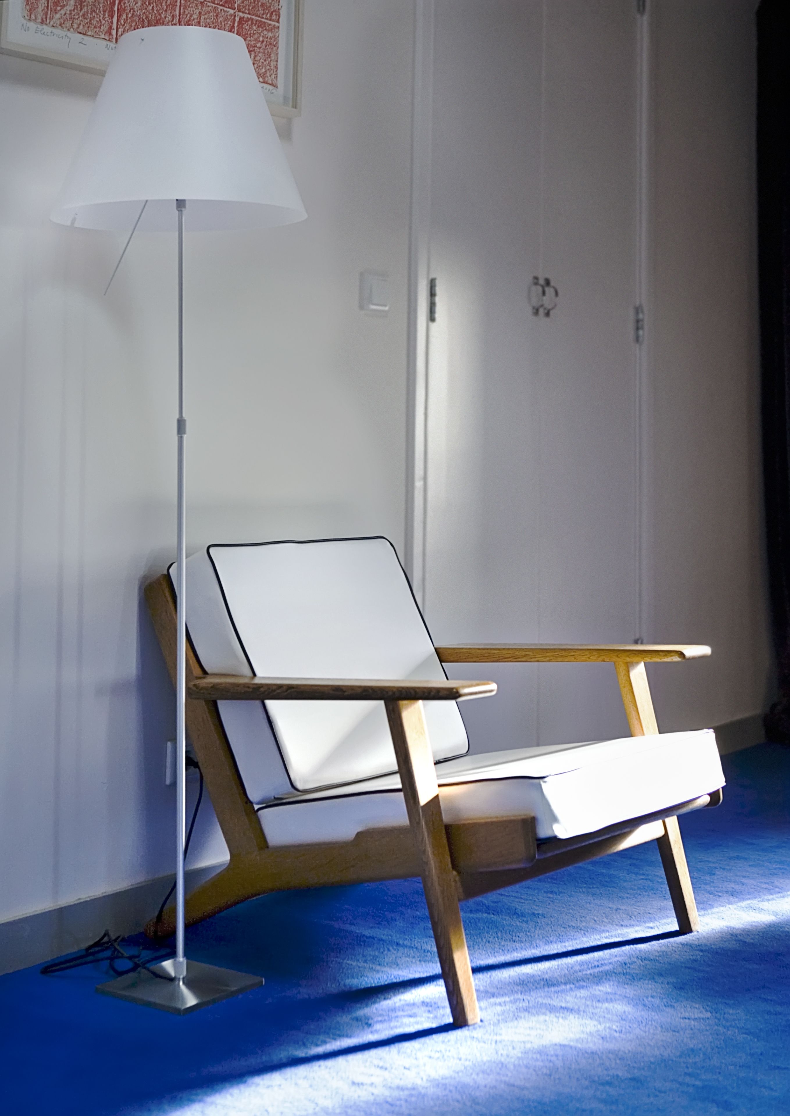 Una habitación moderna con una silla de escritorio blanca, una lámpara de pie y una alfombra azul.