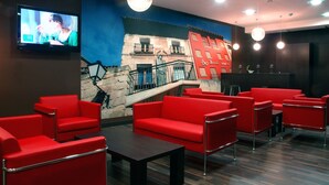 Una hall con sedute rosse, una televisione e un murale raffigurante un edificio.
