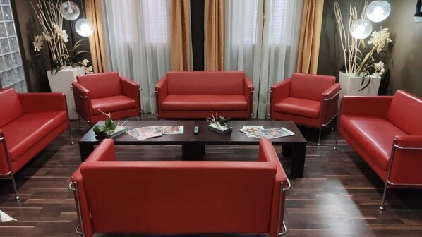 Une pièce dotée d’un parquet en bois foncé, de canapés en cuir rouge, d’une table basse centrale et de plantes décoratives.
