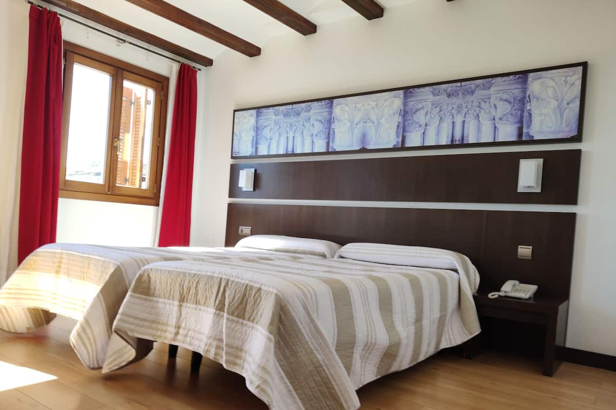 A hotel room with two beds, a wooden headboard, a painting above the beds, and a bedside table with a phone.