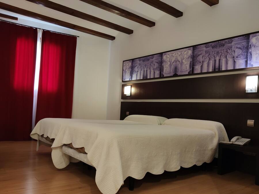 Habitación de hotel con cama, escritorio, silla, cortina roja y un panel decorativo en la pared.