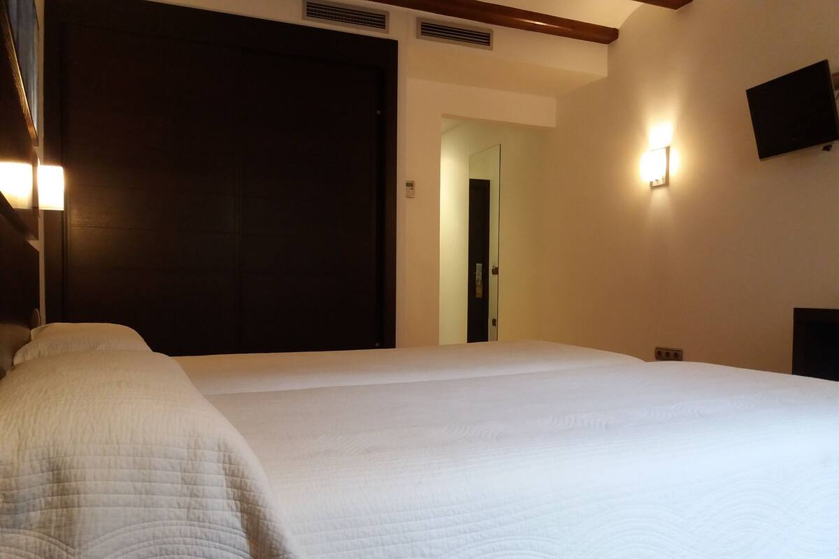 A hotel room with a large bed, a dark wooden door, a wall-mounted TV, and a light fixture.