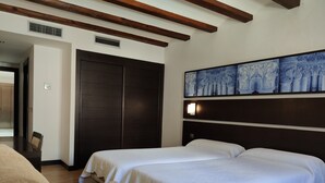Una camera d'albergo con due letti, un armadio in legno scuro, un quadro appeso al muro e un tavolino con una sedia.