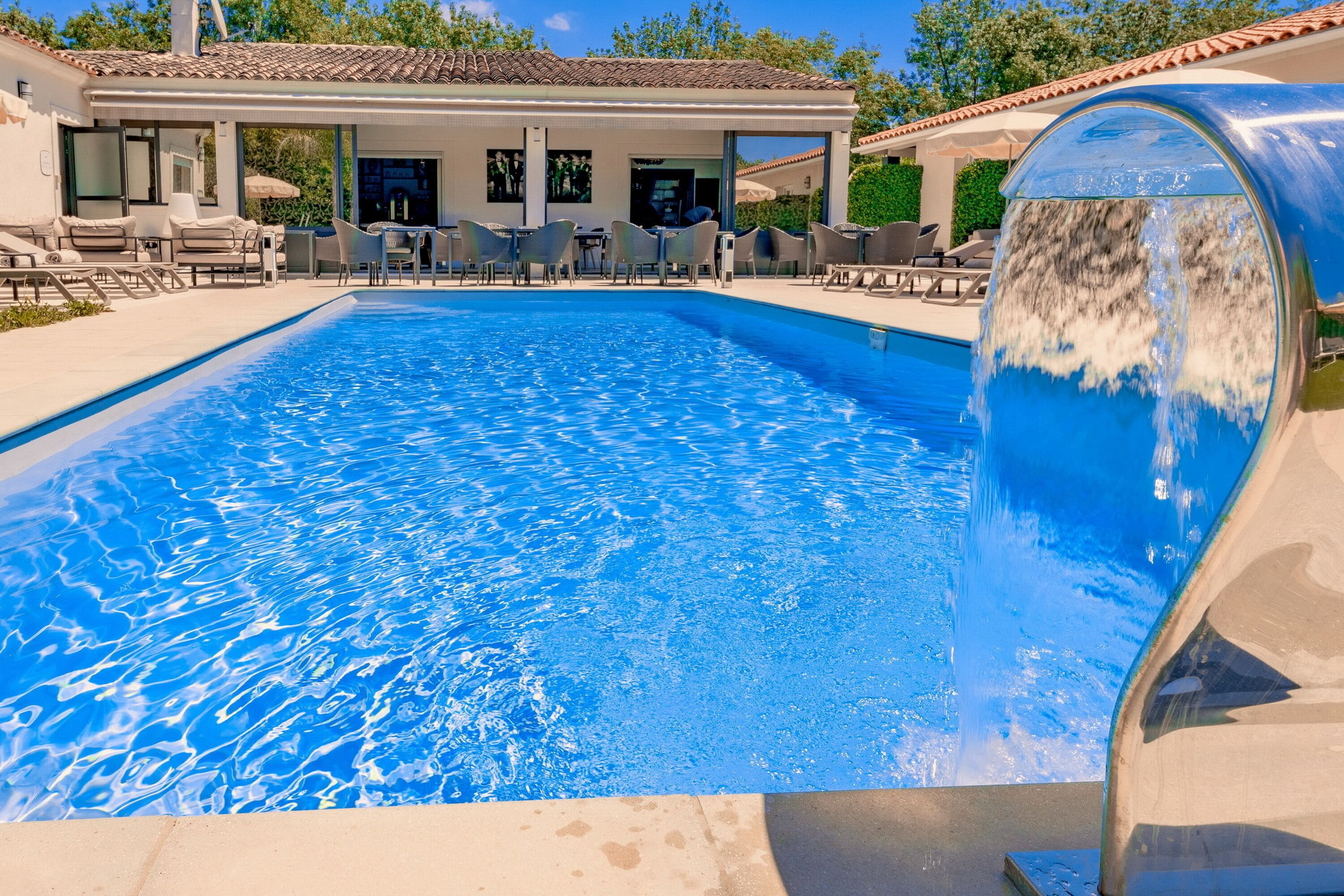 A swimming pool with a waterfall feature, surrounded by lounge chairs and a covered patio area.