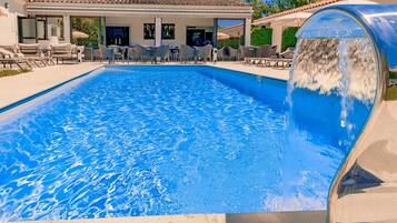 A swimming pool with a waterfall feature, surrounded by lounge chairs and a covered patio area.