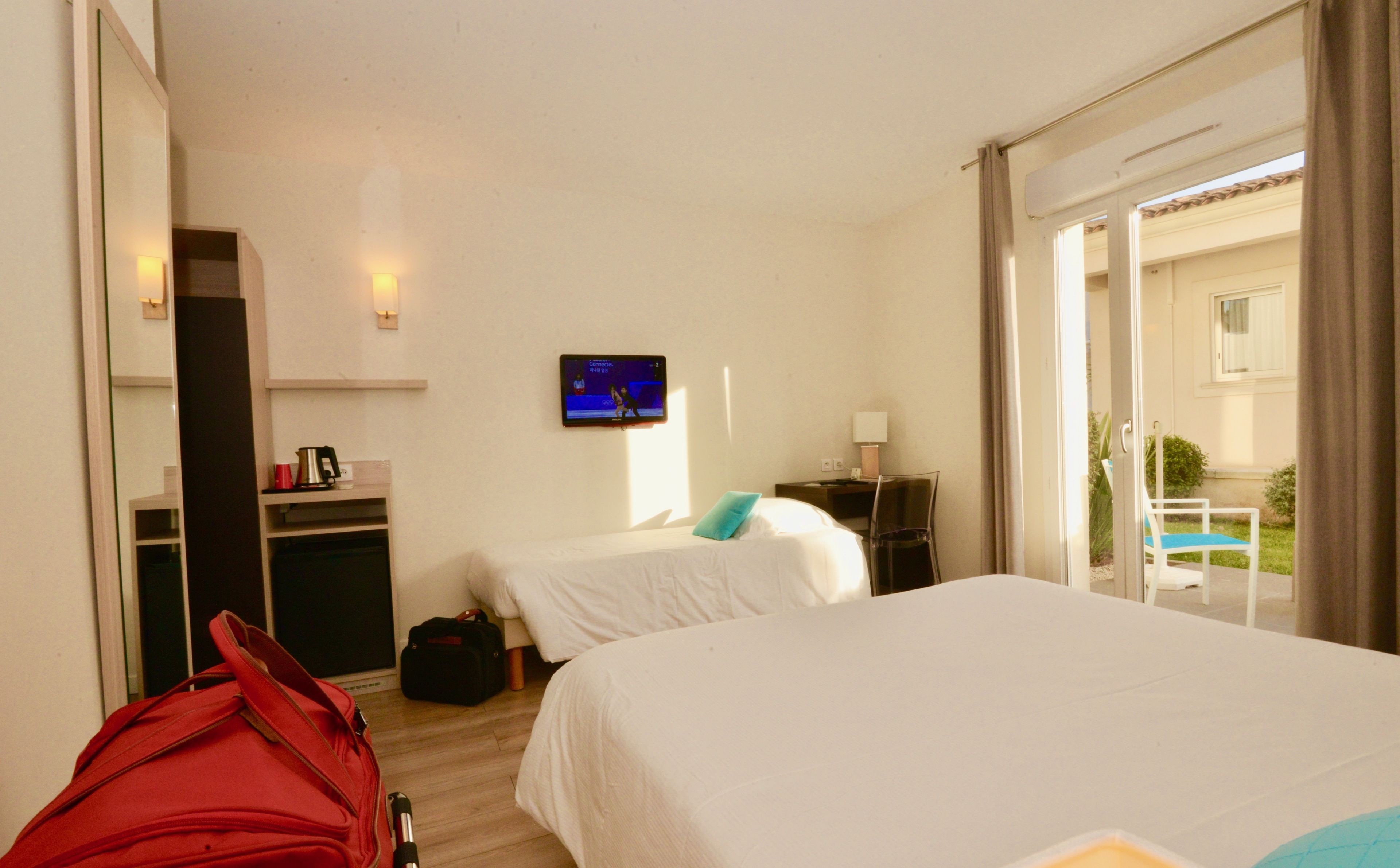 A hotel room with two beds, a TV, a desk, and a suitcase.