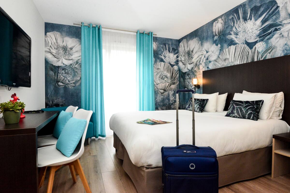 A hotel room with a bed, a desk, a chair, a TV, and a suitcase.