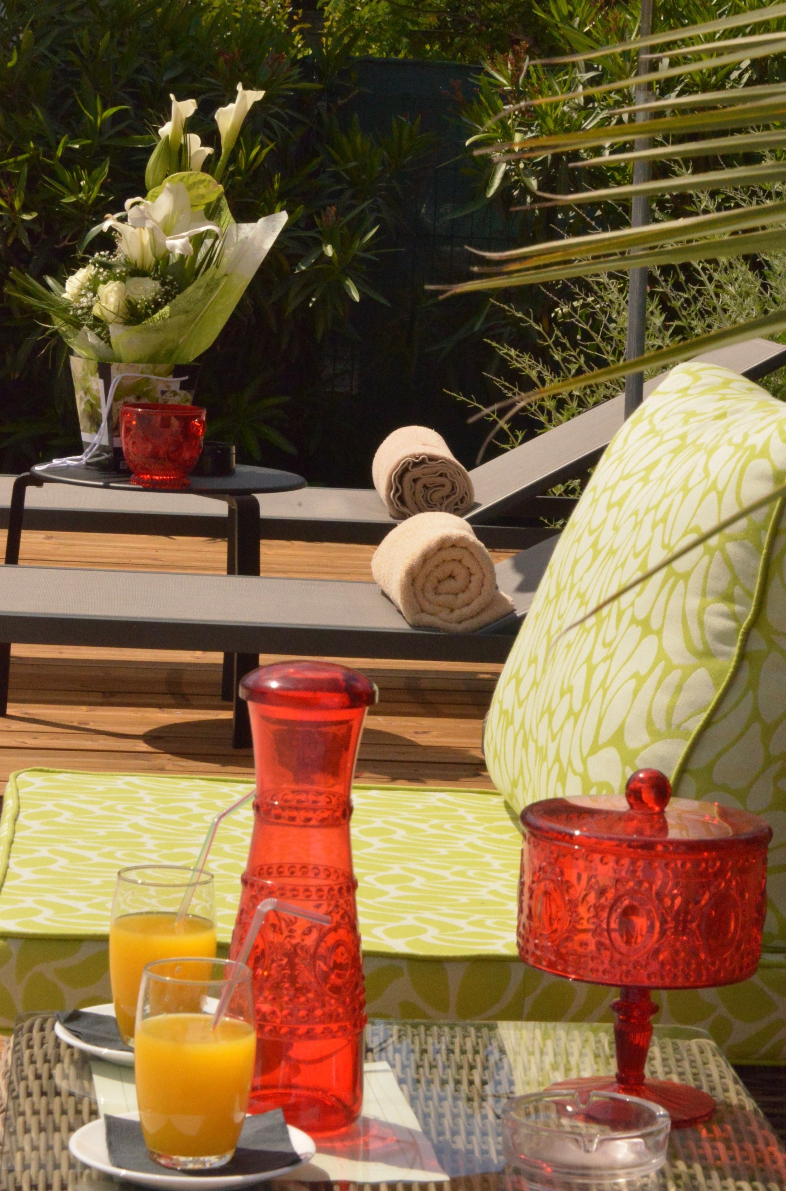 A table set with a red vase, two glasses of orange juice, a candle, and a rolled towel.