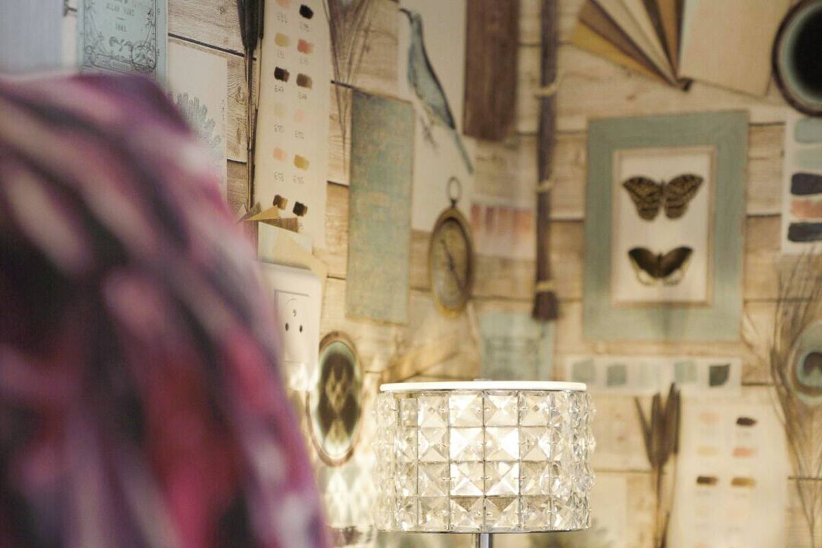 A room with a patterned wall, a lamp, and a partially visible object in the foreground.