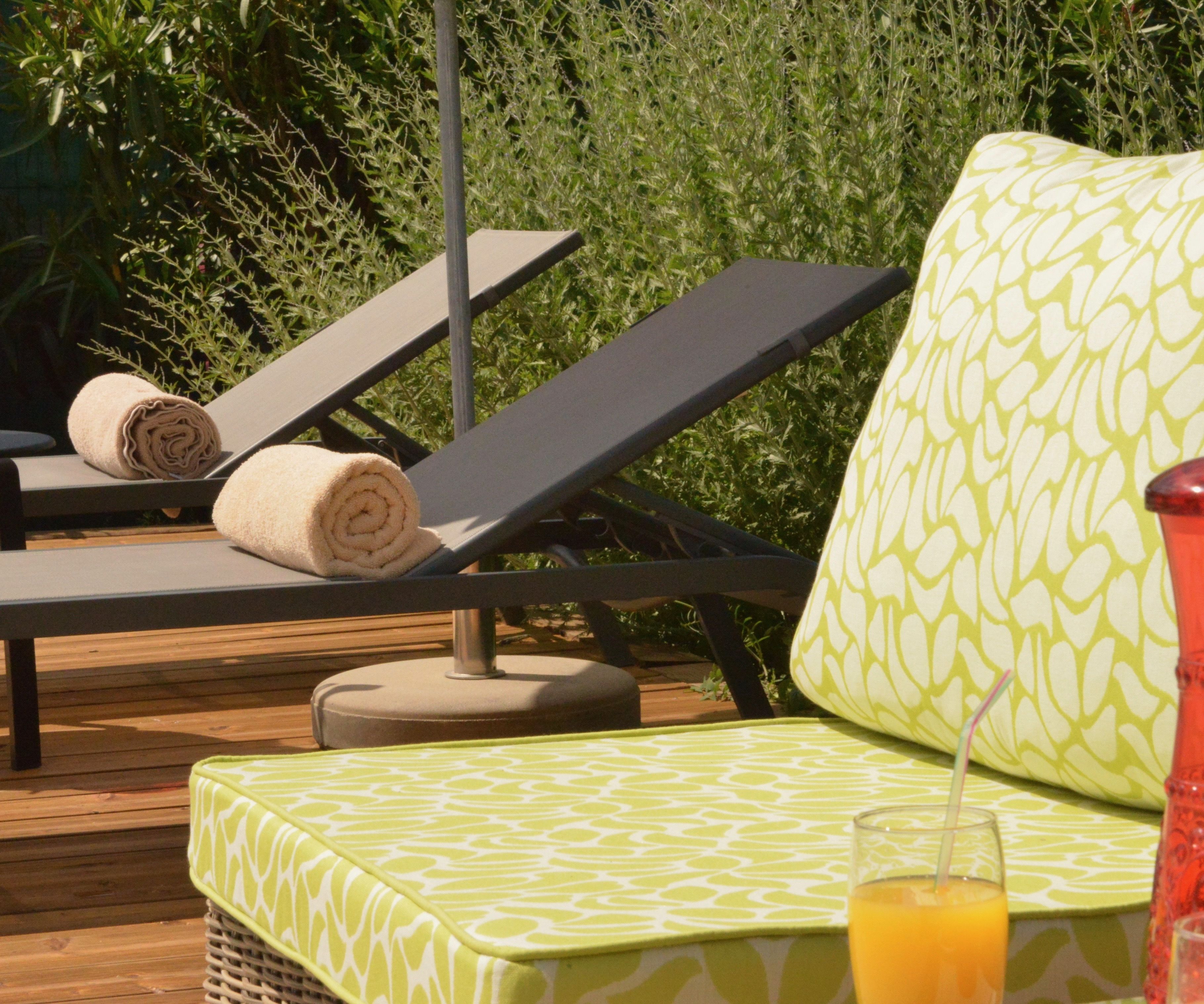 Una tumbona con una toalla, un asiento acolchado y un vaso de zumo de naranja sobre una terraza de madera.