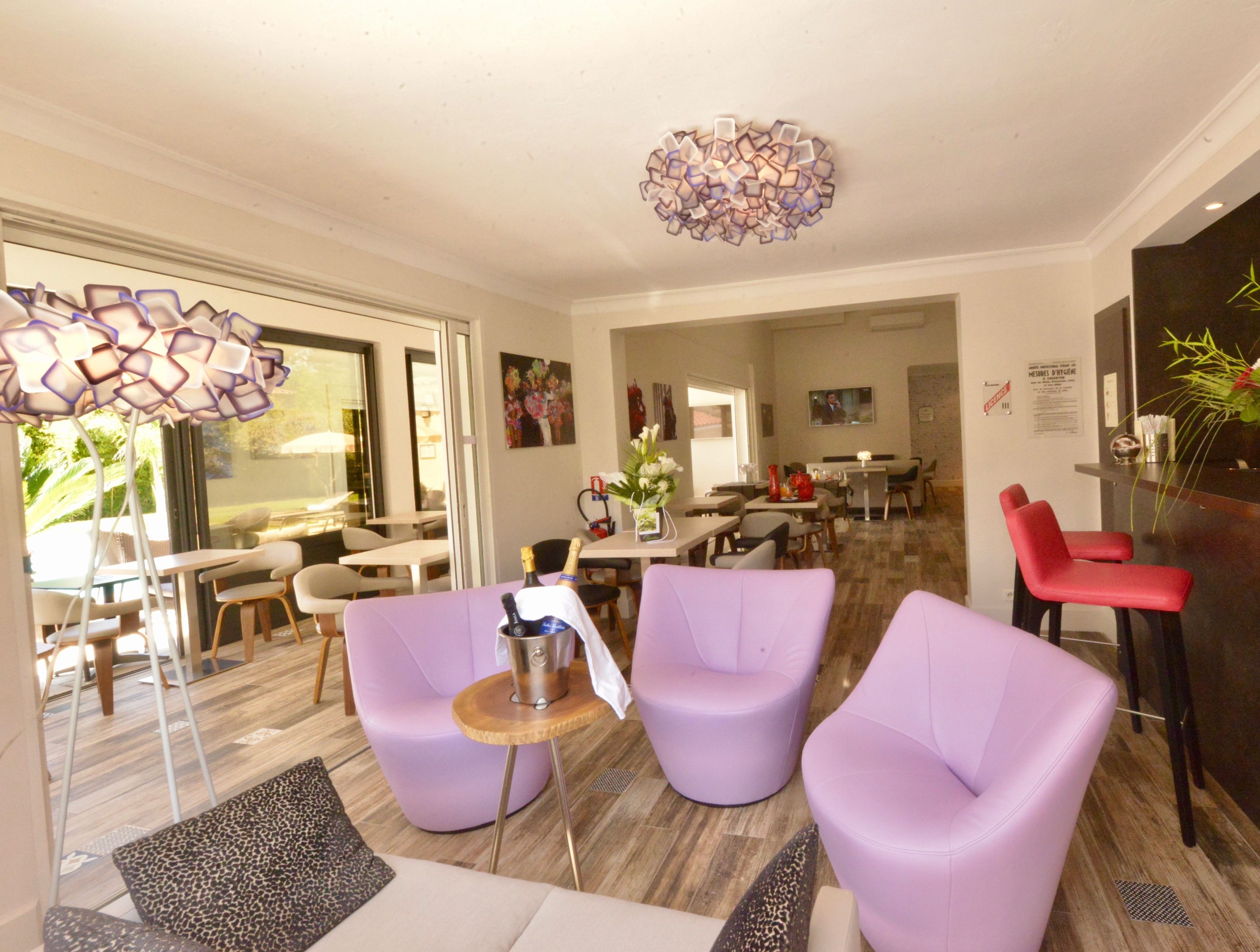 A modern hotel lobby with purple armchairs, a bar area, and a dining space.