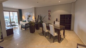 Un salón amplio con una mesa de comedor, sillas y un sofá. Hay plantas en macetas y una estantería.