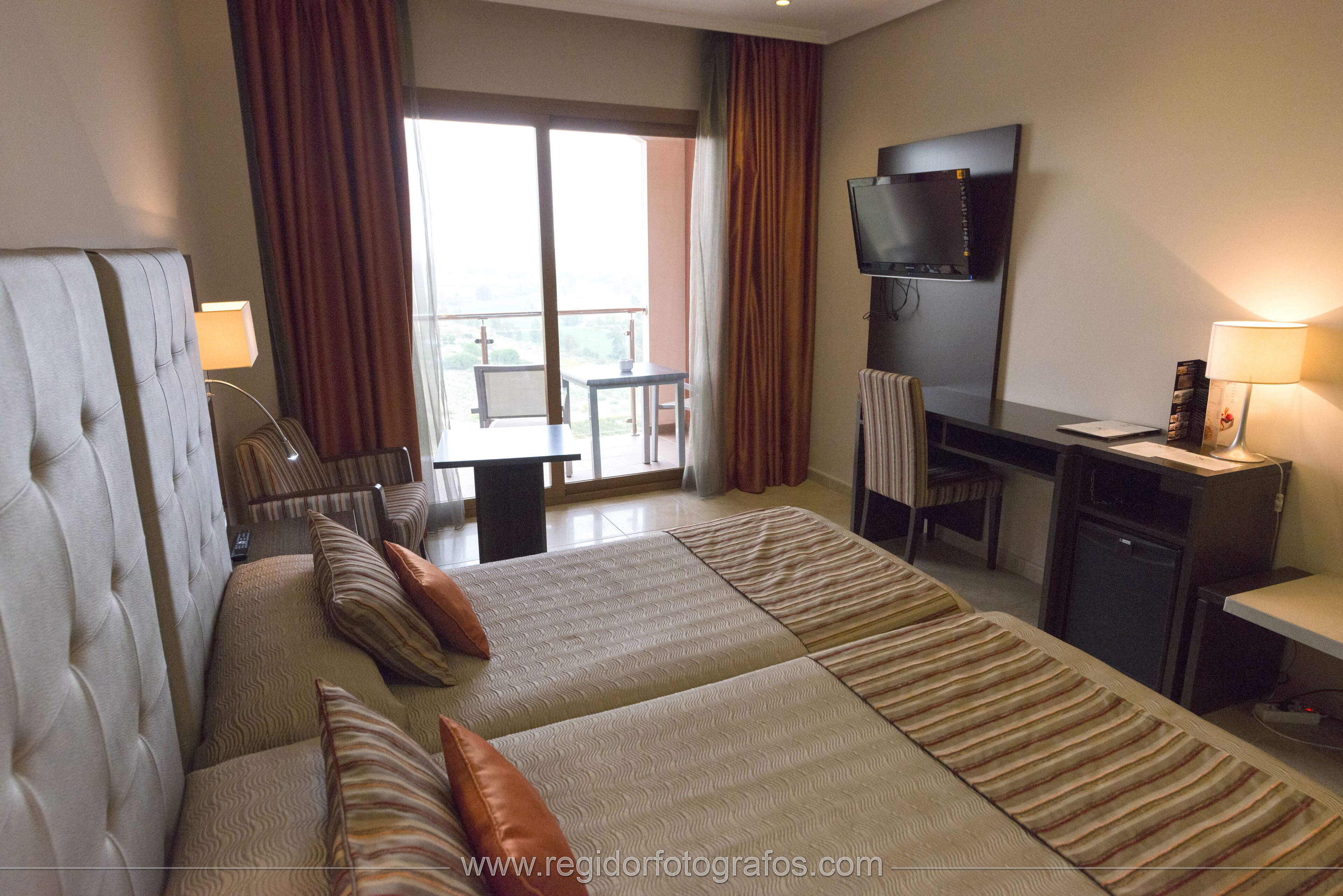 A hotel room with a large bed, a desk, a TV, and a balcony with a view.