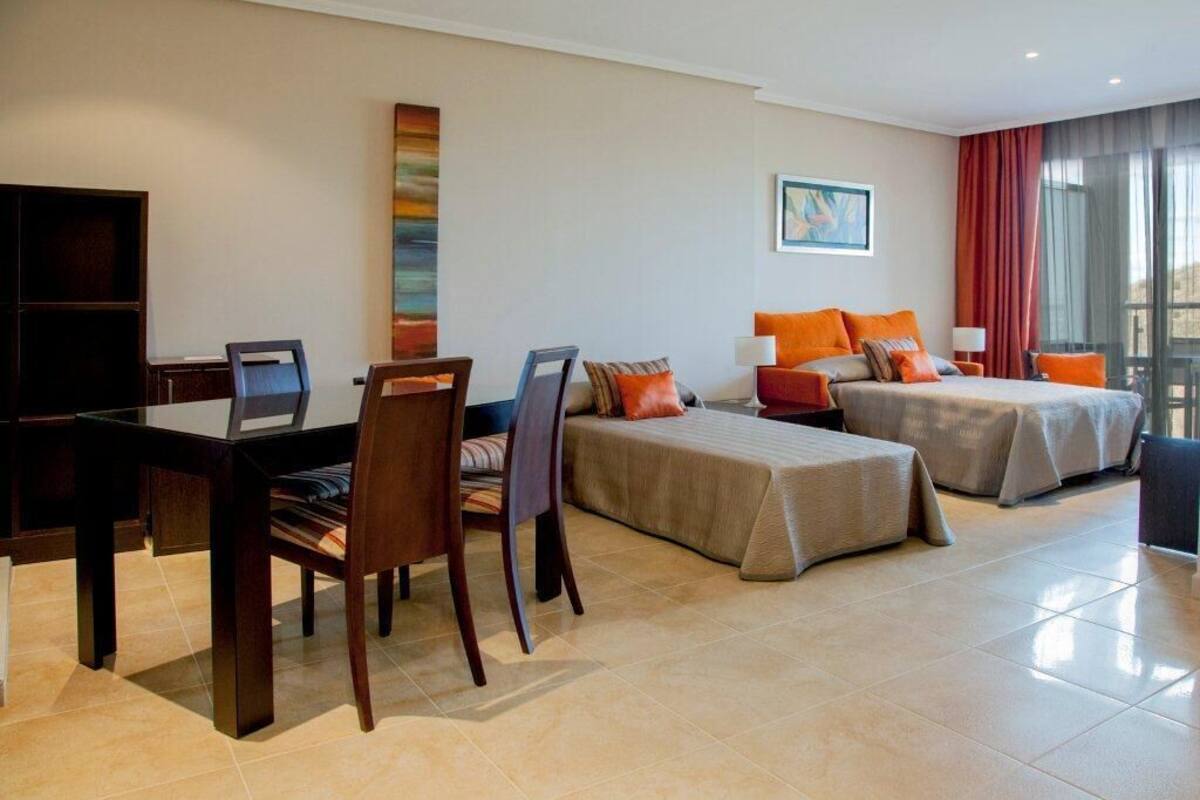 A hotel room with a desk, two beds, a TV, and a large window.