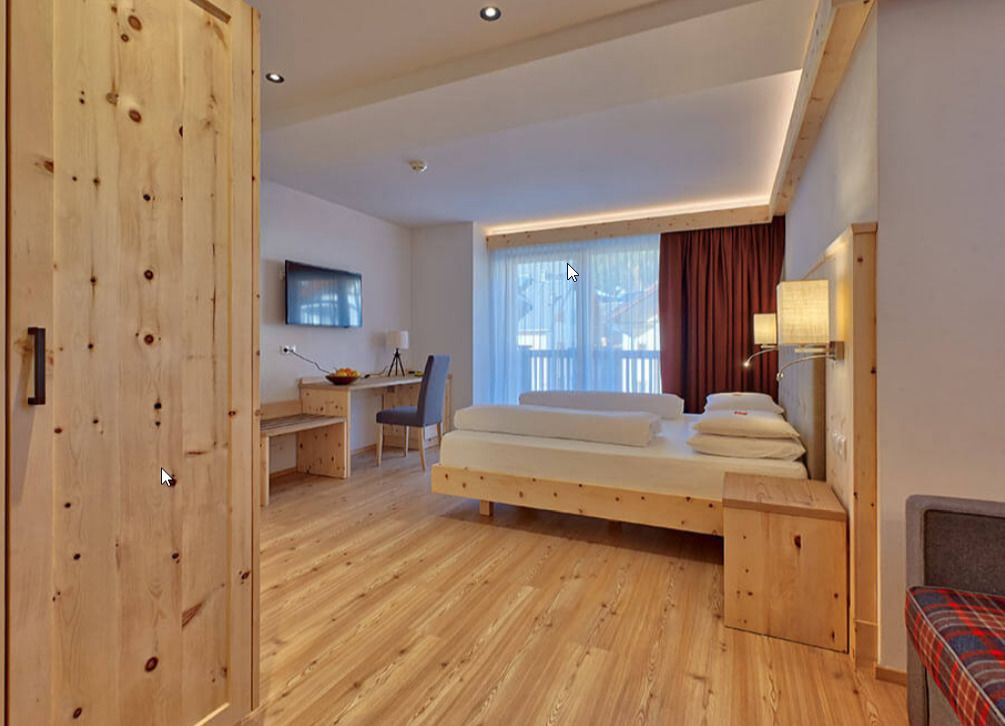A modern room with a wooden floor, a bed with pillows, a desk with a chair, and a TV on the wall.