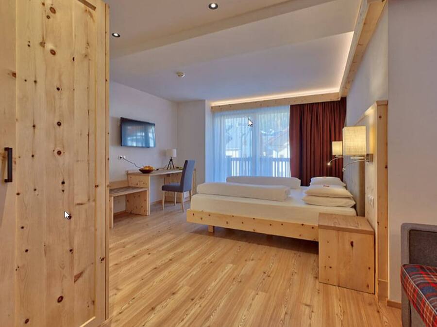 A modern room with a wooden floor, a bed with pillows, a desk with a chair, and a TV on the wall.
