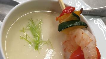 Un tazón de sopa con un camarón y vegetales en brocheta, sobre un plato blanco.