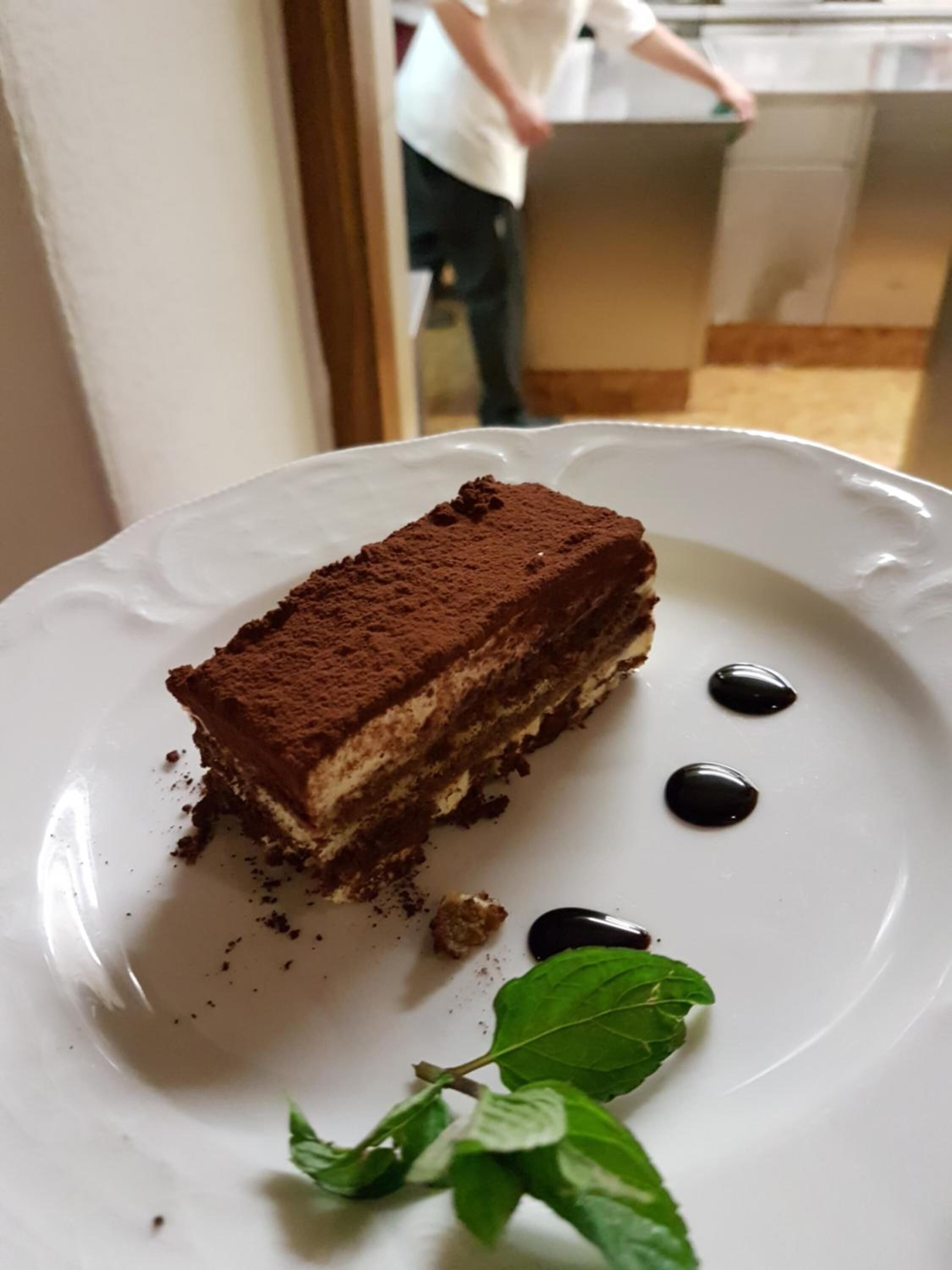 Una porción de postre de chocolate en capas sobre un plato blanco, adornado con una hoja de menta.