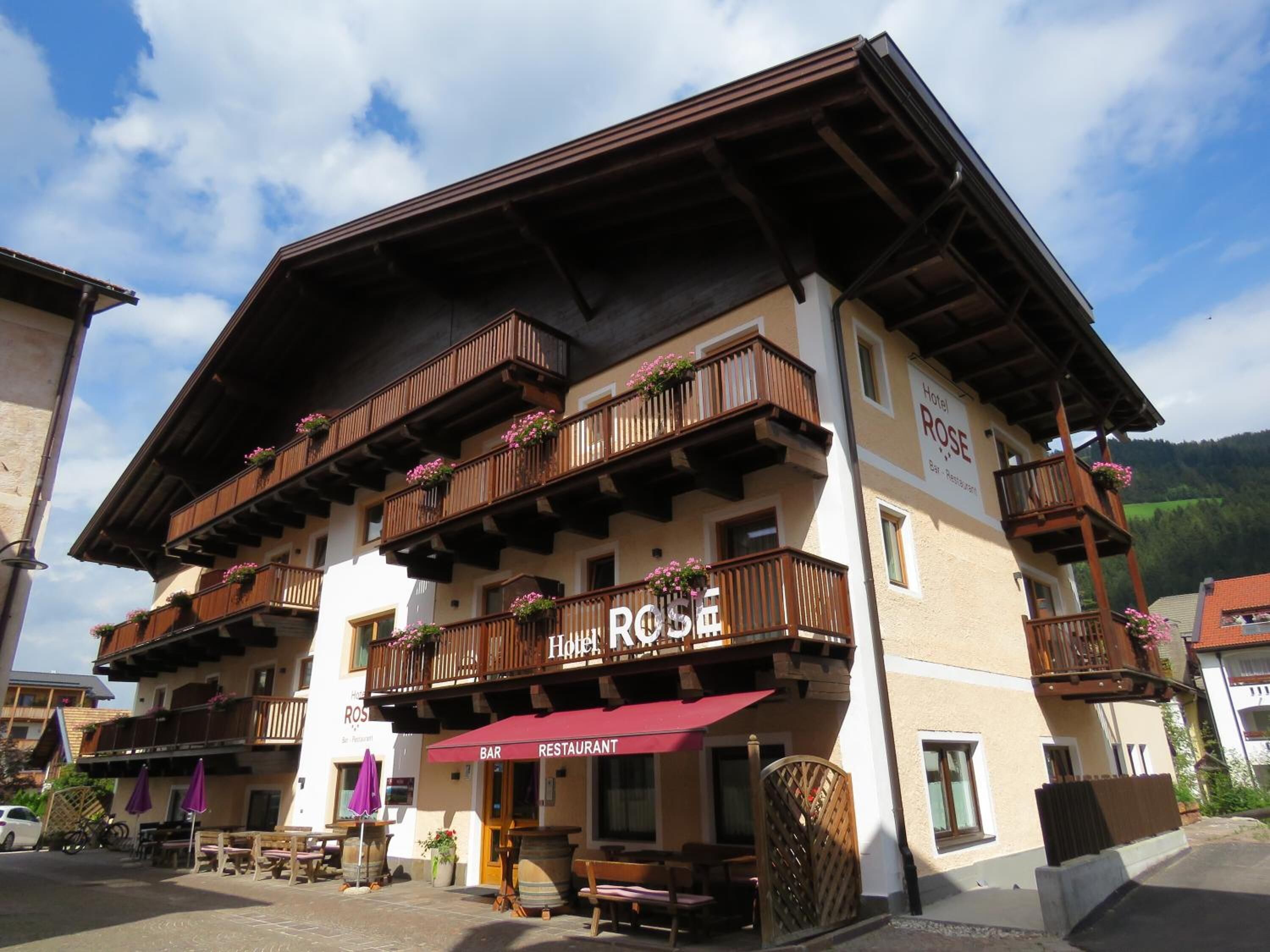 A hotel with multiple balconies adorned with flowers, a bar and restaurant on the ground floor, and a sign indicating it is a hotel named "ROSE".