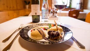 A dessert plate with chocolate and vanilla ice cream on a black and white plate, accompanied by a bottle of water and a glass of red wine on a table. - Hotel Rose (Villabassa)