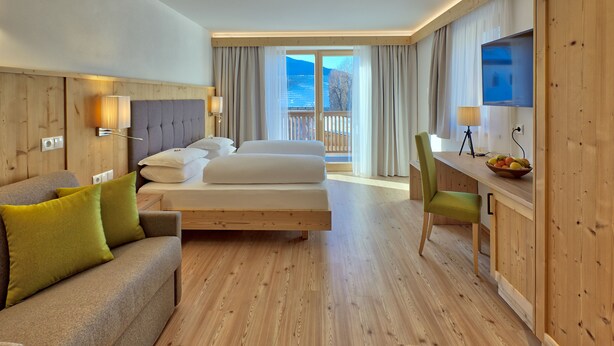 A hotel room with a bed, a sofa, a desk with a chair, and a TV. - Hotel Rose (Villabassa)