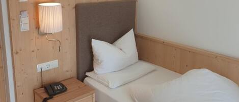 Une chambre avec un lit simple, une tête de lit en bois, une table de chevet avec une lampe et un téléphone.