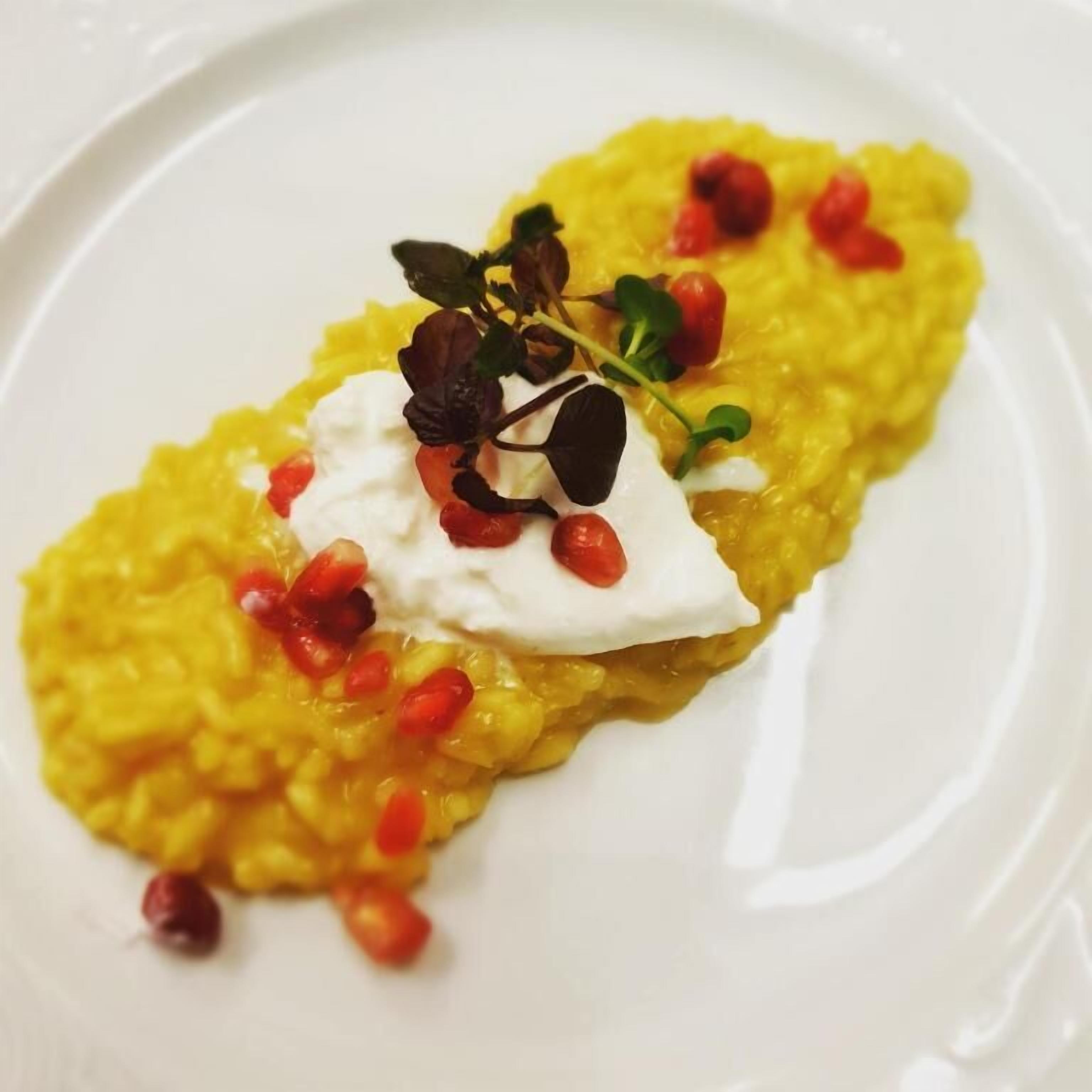 A plate of food with a creamy yellow dish, garnished with red pomegranate seeds and a dollop of white cream, on a white plate.