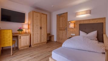 A hotel room with a bed, wooden wardrobe, desk, chair, and a TV mounted on the wall.