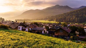 A rural village with traditional houses, a green field, and mountains in the background. - Hotel Rose (Villabassa)