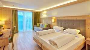 A hotel room with a large bed, a sofa, a desk, and a view of the outdoors. - Hotel Rose (Villabassa)