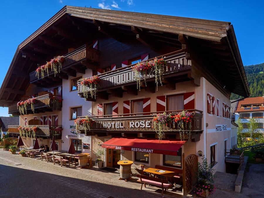 A hotel with outdoor seating, balconies with flower boxes, and a sign reading "HOTEL ROSE."