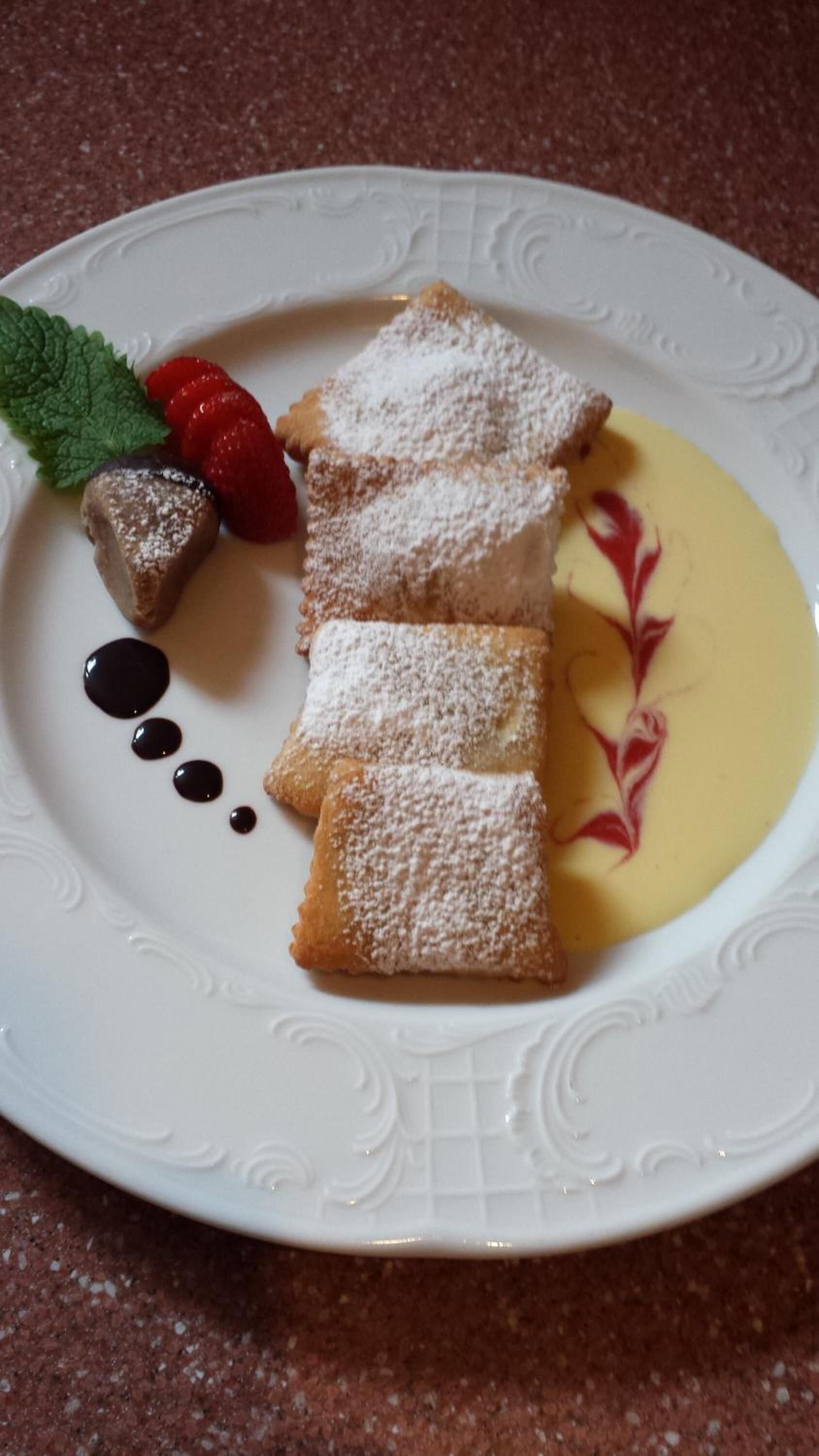 Un plato de postre con azúcar glas, trozos de chocolate y salsa decorativa.