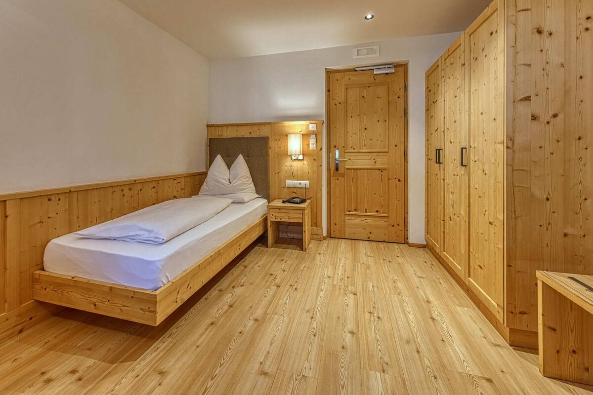 Ein Zimmer mit Holzboden, einem Bett, einem Nachttisch und einem Kleiderschrank.